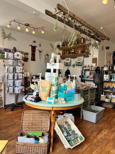 Photo of the inside of the Juniper store; the store looks cozy and welcoming, with warm natural colours. There are displays of postcards and household essentials like cleaning materials.